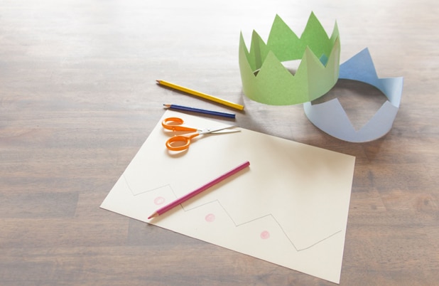 Two paper crowns beside construction paper, scissors and colored pencils.