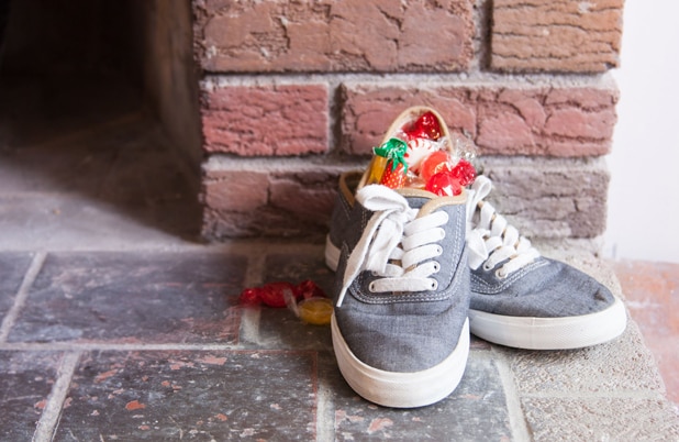 A pair of shoes filled with candy beside a brick fireplace.