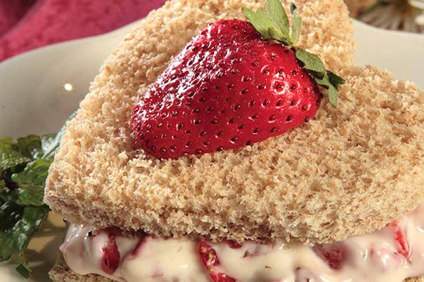 A heart shaped sandwich with cream cheese and strawberry on a white plate.
