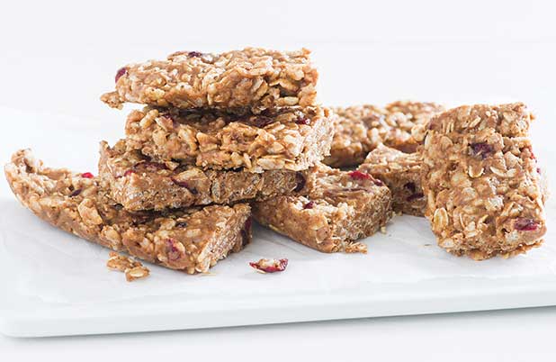 Cereal bars with dried fruit and grains stacked on a white plate.