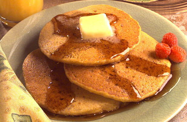 A plate of pancakes with butter, syrup and fresh raspberries.