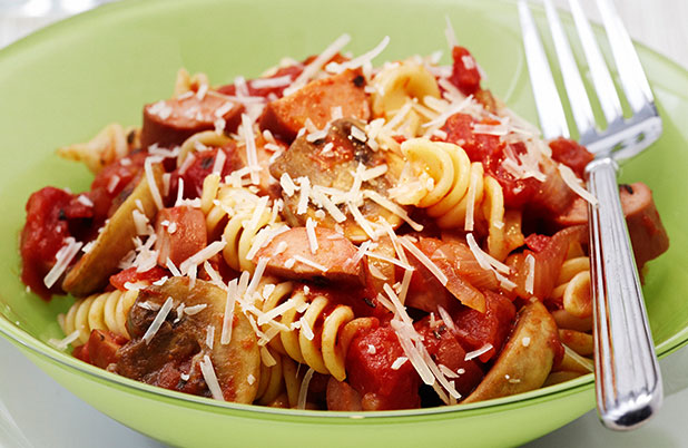 A green bowl of curly pasta with sauce and parmesan beside a fork.