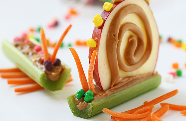 Celery sticks decorated like snails with peanut butter, carrots, apple slices and mini candies.