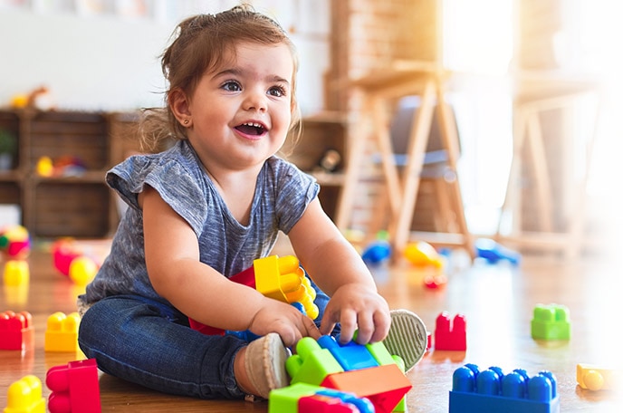 A young girl sits on the floor playing with colorful building blocks.