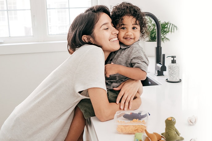 A mom hugs her young son sitting on the bathroom sink.