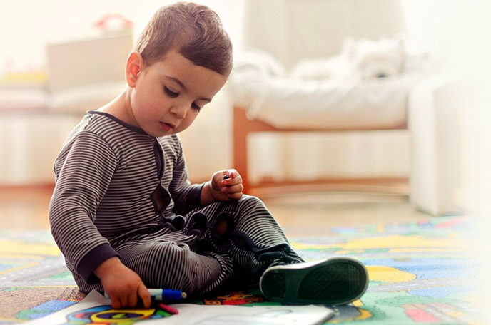 A young boy sits on the floor with markers and a drawing.