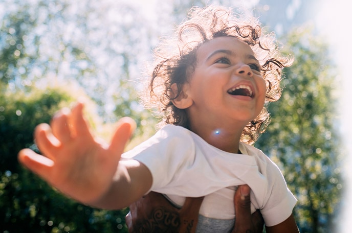 The sun shines on a young boy as his dad lifts him into the air.