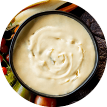 A black bowl of cheesy dip surrounded by blue corn tortilla chips red and green tomatoes and sliced vegetables.