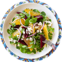 A plate of beet salad beside a fork, pink napkins, and a spoon of vinaigrette.