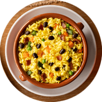 A ceramic bowl of rice and beans on a wooden table surrounded by lime wedges, chili peppers, cilantro, and a fork and napkin.