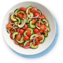 Primer plano de un tazón blanco con una ensalada de pepinos sobre un fondo azul.