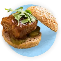 Close up of a meatloaf sandwich on a hamburger bun with pickles, on a blue background.