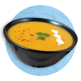 close up of a butternut squash soup in a black bowl, on a blue background.