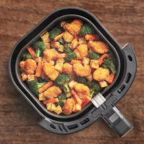 An open air fryer tray filled with breaded chicken pieces and mixed veggies, all on a wooden background