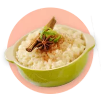 Un tazón verde lleno de pudín de arroz adornado con ramas de canela sobre un círculo naranja.