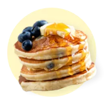 stack of pancakes with butter, syrup and blueberries on a yellow circle.