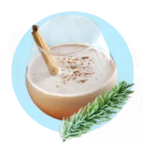 Un vaso lleno con coquito y una rama de canela cerca de pinocha sobre un círculo celeste.