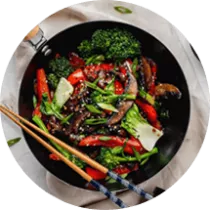 Chopsticks sit on a pot filled with broccoli, mushrooms, peppers, bok choy and sesame seeds.