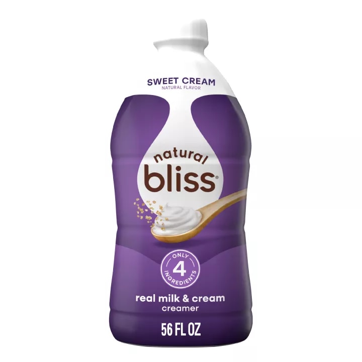 Large white bottle of natural bliss Sweet Cream flavored Creamer with a purple label above a spoon of sugar and swirl of milk