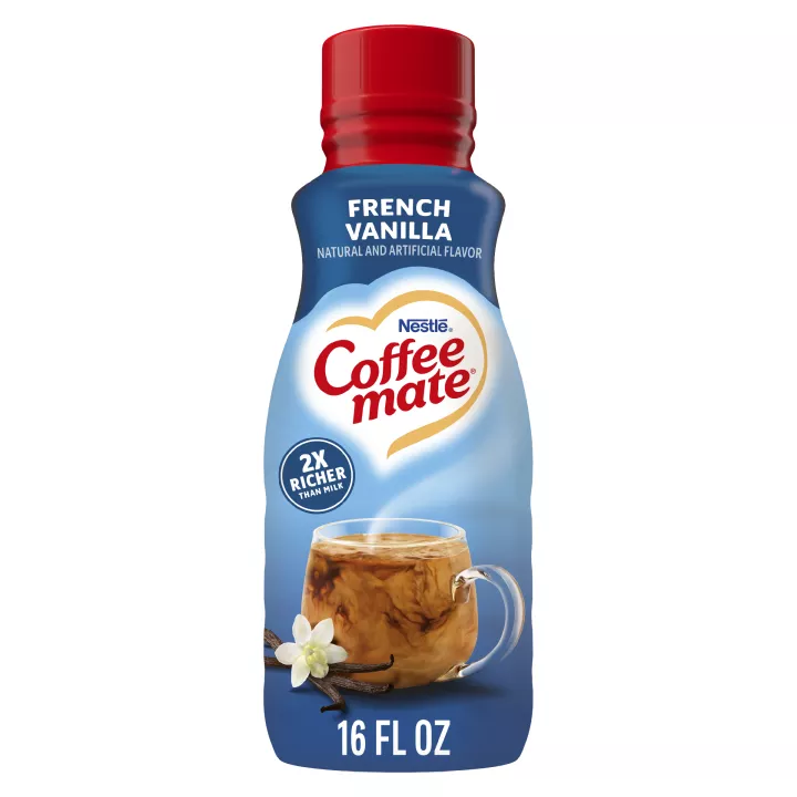 Una botella azul de creamer Coffee mate French Vanilla con una tapa roja y una etiqueta azul sobre una taza de café y vainas de vainilla.